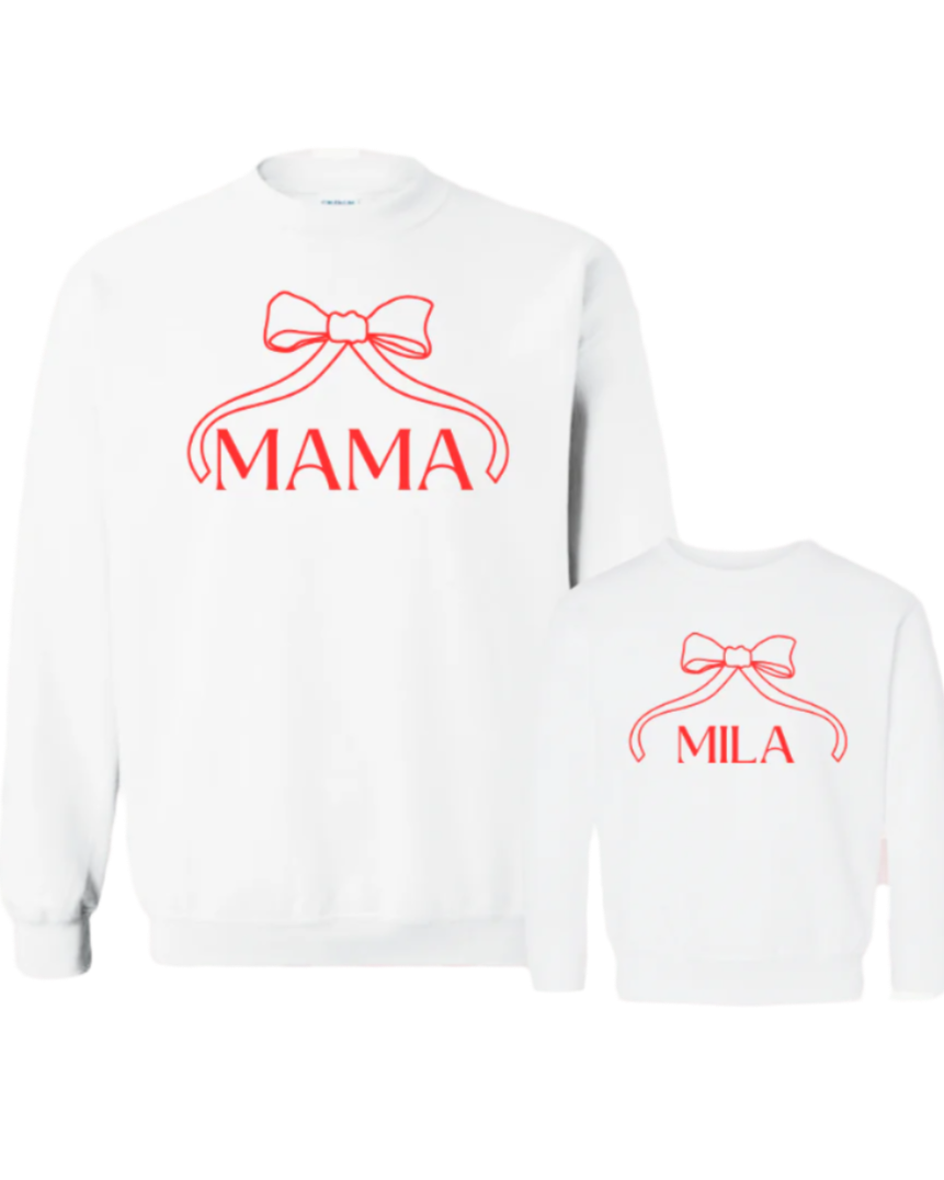 Two white crewneck sweatshirts with red text, one saying 'MAMA' and a bow illustration, and the other saying 'MINI' with a smaller bow illustration, on a checkered background.