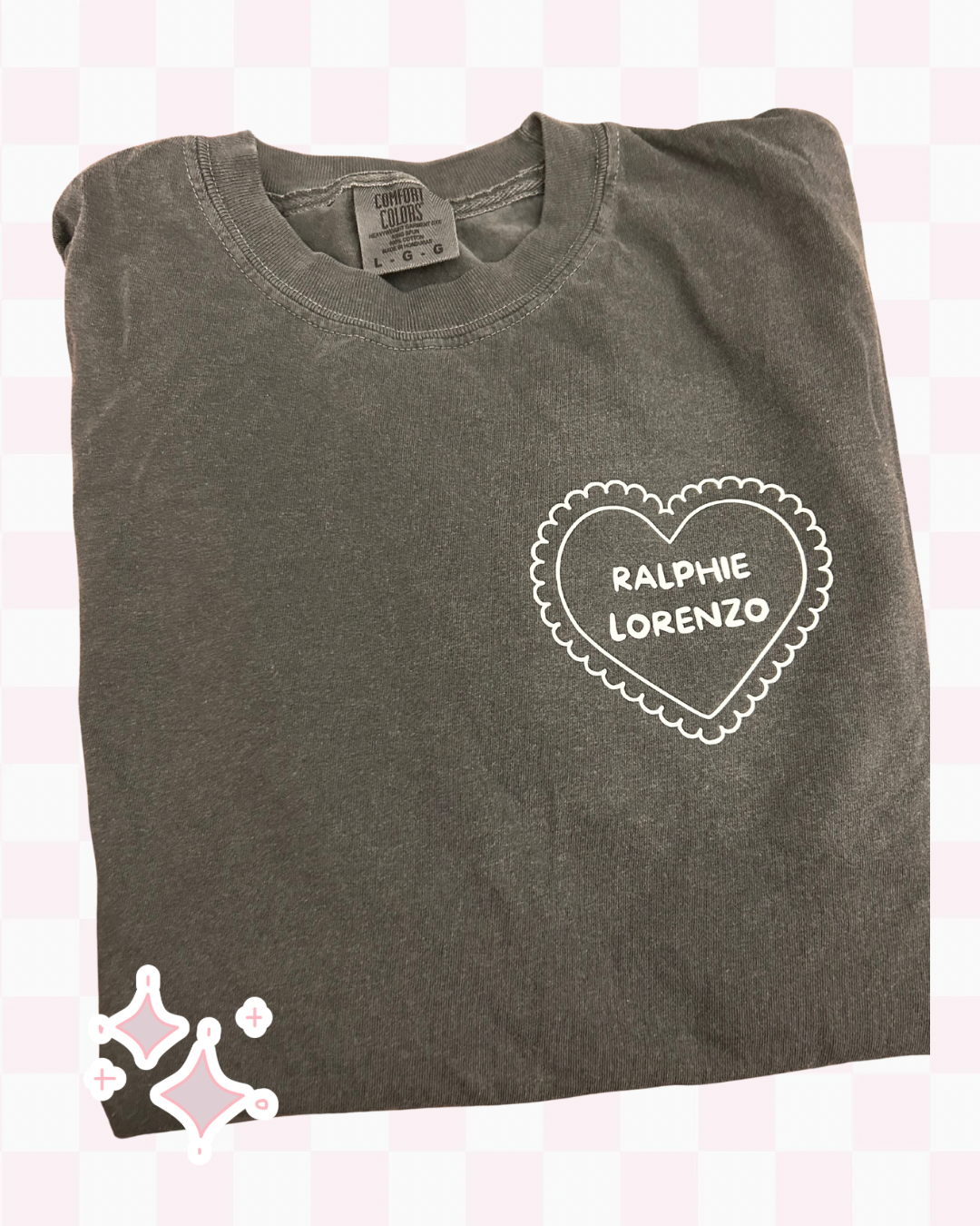 Folded gray t-shirt with a heart-shaped logo and text on a light pink background